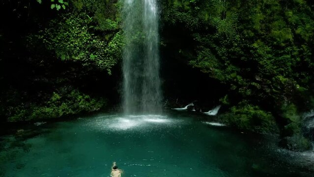 aerial view of man swimming towards waterfall