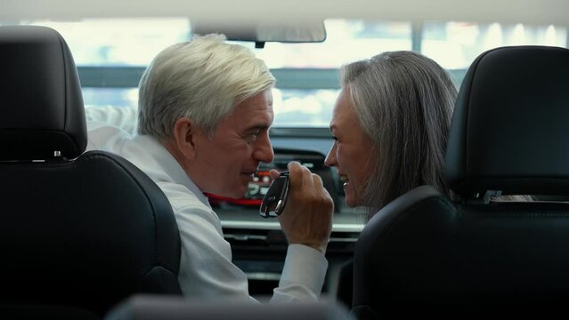 A mature Caucasian couple is sitting in a new car. Elderly man holding car keys. 