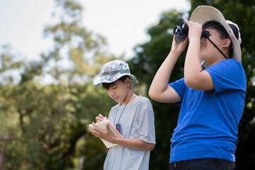 Asian boys holding binoculars and watching birds which fying on sky, insects, forest animals and living things which crawling and jumping on the branches and on the underside of trees in tropical park