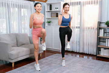 Fototapeta na wymiar Energetic and strong athletic asian woman with workout buddy running in place at her home. Pursuit of fit physique and commitment to healthy lifestyle with home workout and training. Vigorous