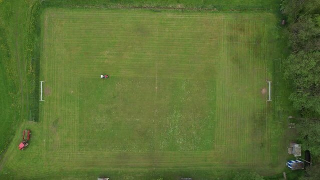 football pitch cutting machine aerial video real time, cutting green grass on a football field,sport concept,Person with pruner cutting the grass inside a football stadium with a tractor