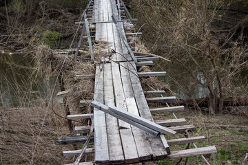 A broken pedestrian suspension bridge in the countryside after a spring flood