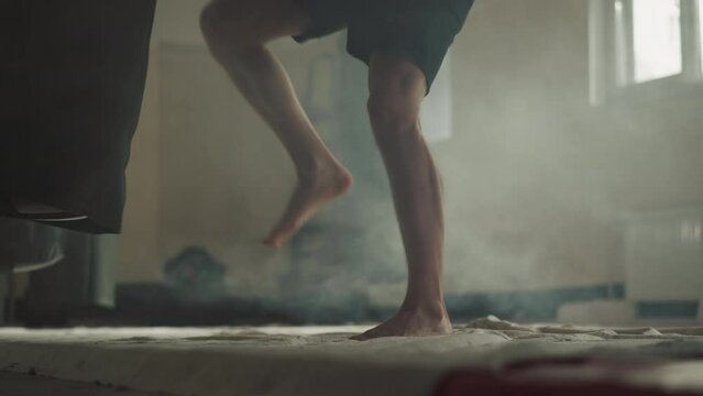 Barefoot man hits punching bag by knees in gym closeup. Professional sportsman trains leg kicking with heavy equipment in sports club slow motion