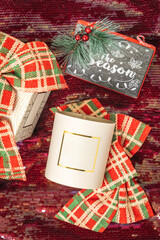 Product photography of a cream colored candle vessel surrounded by plaid Christmas colored bows and...
