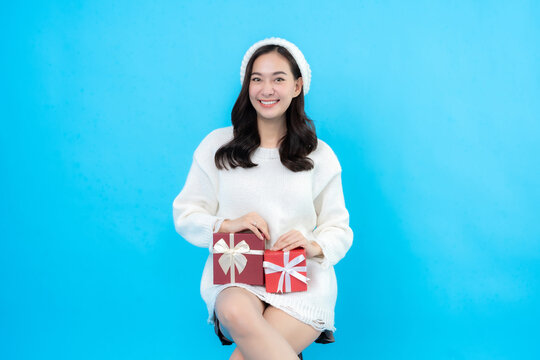 Asian woman with long hair Preparing to celebrate New Year and Christmas, holding a gift box tied with a ribbon on it, smiling cutely, taking pictures against a blue backdrop in the studio.
