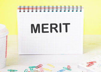 Merit the word is written on a blank sheet in a notebook standing on a table on a yellow background