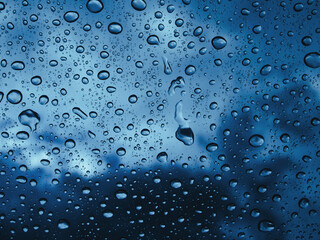 Raindrops water on the window glass against the background of dark clouds. Stormy weather in rainy season. Moody blue.