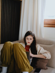 A woman lies on a couch with a laptop and stares pensively into the screen training a freelancer at work, a real lifestyle without retouching.