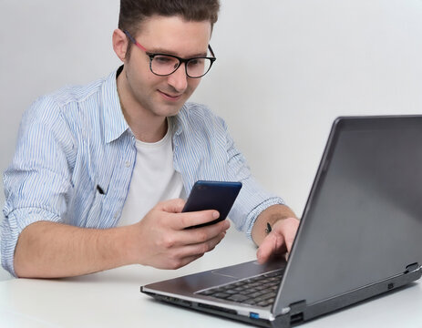 Caucasian man in an office shopping online using phone and laptop. Mobile payment and banking concept. 