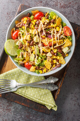 Taco salad is a warm salad made with chili beans, spicy ground beef, corn, lettuce, cheese and avocado closeup on the plate on the table. Vertical top view from above