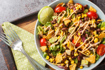 Beef Taco Salad made with beans, corn, nacho chips, lettuce, tomato, onion, cheese and avocado closeup on the plate on the table. Horizontal top view from above