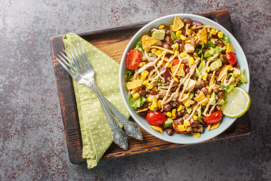 Ground beef taco salad with nacho chips, vegetable salsa, cheese dressed with cream sauce close-up on a plate on the table. Horizontal top view from above