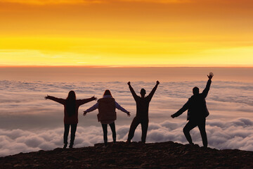 Happy friends or tourists are greeting sunrise or sunset high on the mountain above the clouds
