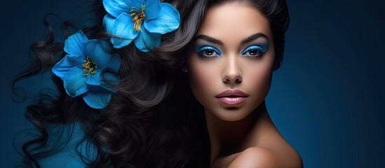 Fototapeta premium The beautiful Hispanic woman with a sexy blue flower in her hair had a background as a spa girl, and her stunning face with flawless makeup made her look like a model known for her feminine and