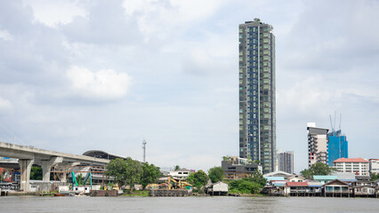 Fototapeta na wymiar A picture of a cityscape in the suburbs with a river flowing through By the river bank There are small buildings densely populated. And there are 2 condominium buildings.