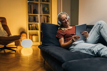 Beautiful young woman sitting on a sofa and using digital tablet in the evening.