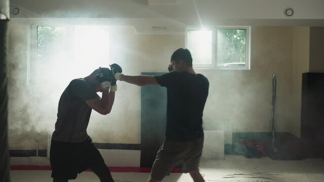 MMA fighters training sparring in sports club. Young strong kick-boxers fight exercising in empty misty gym. Martial arts masters performance