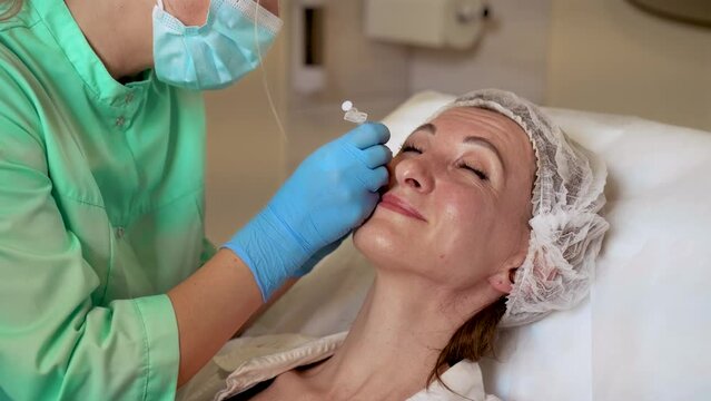 Adult smiling woman gets neurotoxin injection in her face at beauty salon for wrinkles lifting and skin care. Professional cosmetologist doing injection with neurotoxin for rejuvenation face skin