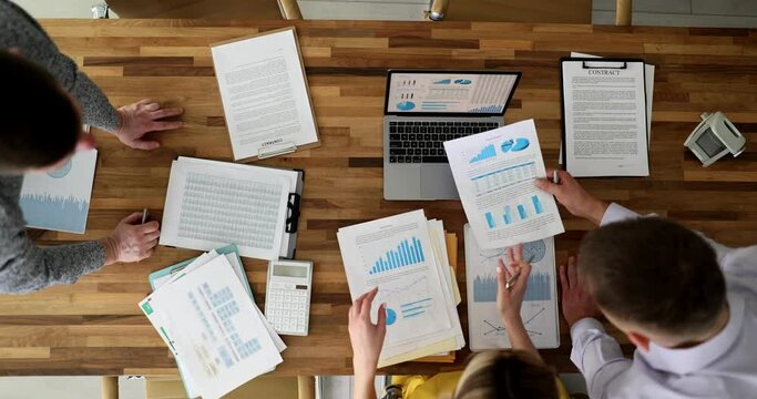 Businesspeople studying documents with graphs at table in office at business meeting top view 4k movie slow motion. Strategies in business teamwork concept