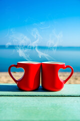 two heart shaped mugs with tea on the seashore
