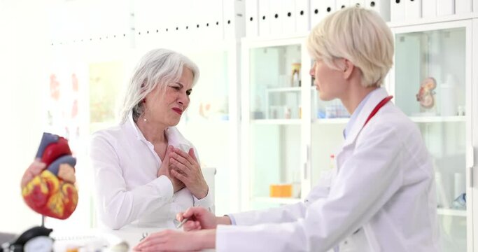 Elderly female patient complaining of pain in heart to doctor in clinic 4k movie slow motion. Symptoms of ischemic heart disease in aged people concept