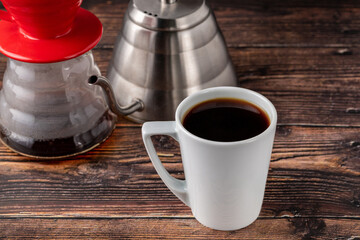 A cup of coffee and third generation pour over coffee brewing equipment on wooden floor