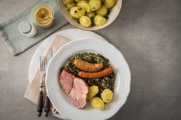 Oldenburger Grünkohl mit geräucherter Kohlwurst, Pinkel, Kassler Nacken, Kartoffeln, Senf, Petersilie auf Teller und hell grau Stein Hintergrund