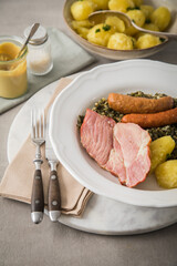 Oldenburger Grünkohl mit geräucherter Kohlwurst, Pinkel, Kassler Nacken, Kartoffeln, Senf, Petersilie auf Teller und hell grau Stein Hintergrund