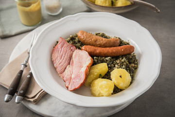 Oldenburger Grünkohl mit geräucherter Kohlwurst, Pinkel, Kassler Nacken, Kartoffeln, Senf, Petersilie auf Teller und hell grau Stein Hintergrund