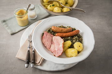 Oldenburger Grünkohl mit geräucherter Kohlwurst, Pinkel, Kassler Nacken, Kartoffeln, Senf, Petersilie auf Teller und hell grau Stein Hintergrund