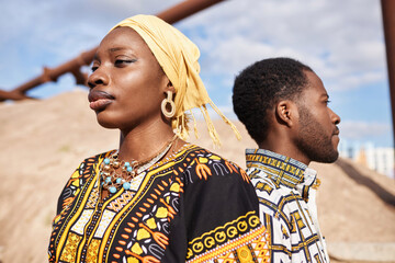 Close up portrait of traditional African American couple standing back to back in desert sun, focus...