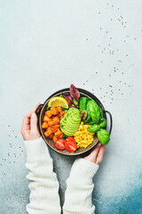 Woman's hands hold a bowl of Buddha: from pumpkin, avocado, corn and tomatoes, Healthy vegetarian...