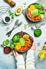 Female hands in a sweater hold a bowl of salad, healthy lunch: pumpkin, avocado, corn and tomatoes, clean eating, vegan food concept. Top view - obrazy, fototapety, plakaty
