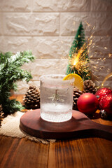 Snow Globe Cocktail. Christmas drink, creative festive beverage in drink glass decorated with rosemary sprig like a christmas pine tree, citrus slice and christmas sparkler.