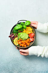 Woman's hands hold a bowl of Buddha: from pumpkin, avocado, corn and tomatoes, Healthy vegetarian dinner.