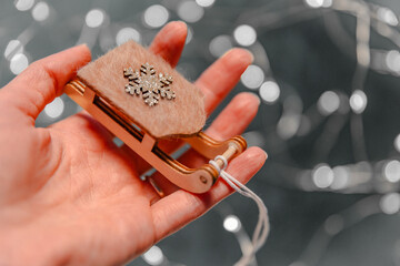 Charming Christmas wooden sleigh held in a woman's hand against a bright backdrop adorned with...