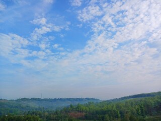 The view of the plantations is green and beautiful, there are blue clouds. See the view of the hills with blue clouds.