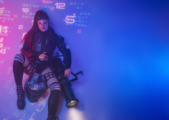 A woman in a futuristic tactical black suit lies on the floor, with a motorcycle helmet and a massive projector lying beside her, against a backdrop of projected digital symbols