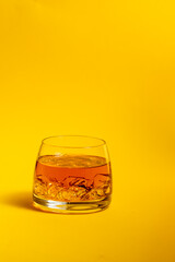 glass of whiskey with ice on a yellow background, exclusive alcoholic drink
