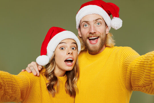Close up merry young couple two friends man woman wear sweater Santa hat posing doing selfie shot pov on mobile cell phone isolated on plain green background. Happy New Year Christmas holiday concept.
