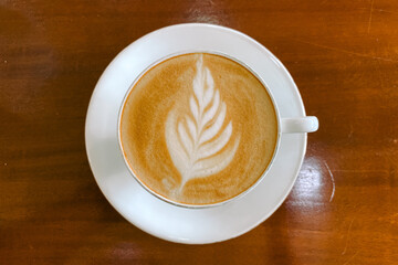 Rosetta tulip latte art in a cup of coffee with wooden table background top view