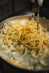 Close up of cook stirring spaghetti with parmesan cheese on a pan.