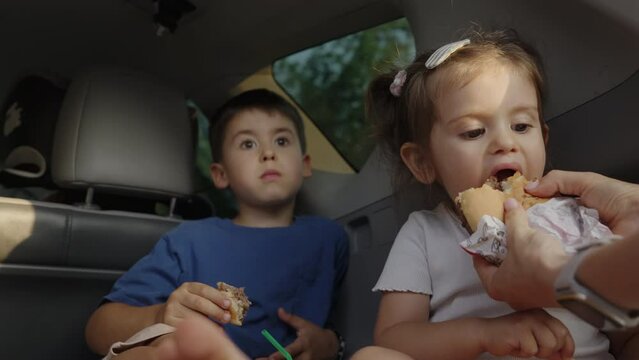 Two adorable kids, teenager boy and funny little girl, brother and sister, sitting in the trunk of a car eating sandwiches enjoying family weekend.