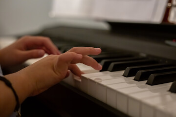 Obraz premium Close up of the hands of a girl playing piano. Hands of little girl playing piano, selective focus. Hands of concentrated girl playing electronic piano at home