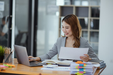 Businesswoman working with stack of documents papers and laptop sitting at office desk.