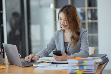 Accounting asian woman use smartphone and laptop at office desk in office, Accounting businesswoman online working concept.