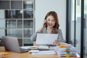Obraz premium Accounting asian woman use smartphone and laptop at office desk in office, Accounting businesswoman online working concept.