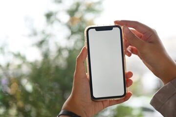 Woman hands holding smartphone with white empty screen on nature background