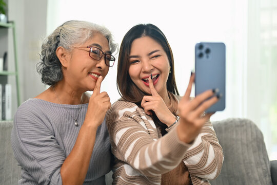 Happy young Asian woman taking selfie picture on smartphone with happy mature mother