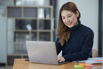 Happy young asian businesswoman with laptop sitting at workplace in modern office.